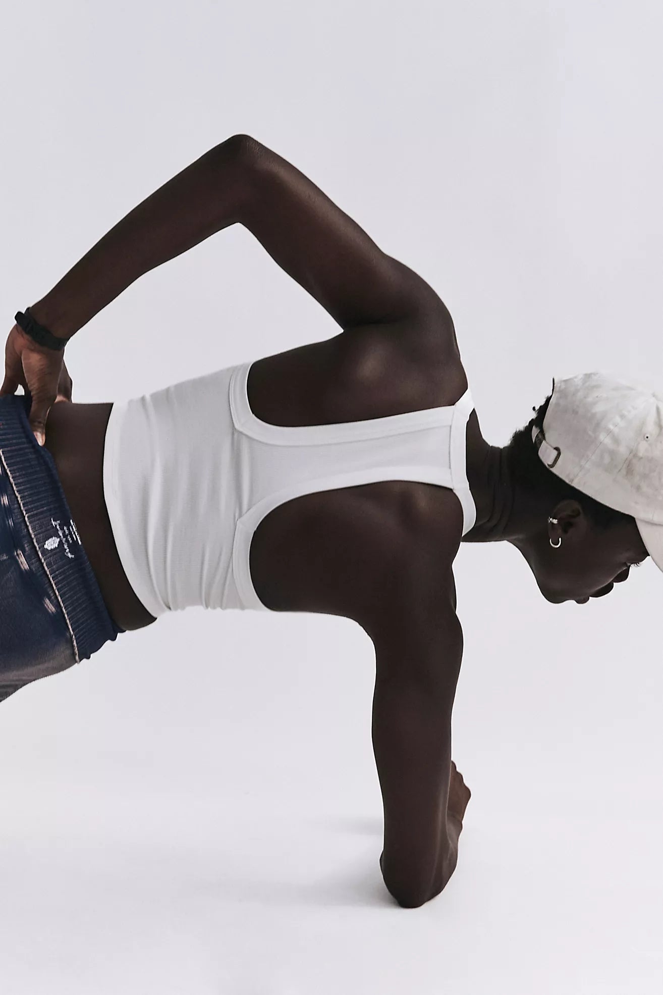 Person wearing a white tank top and denim shorts on a light gray background