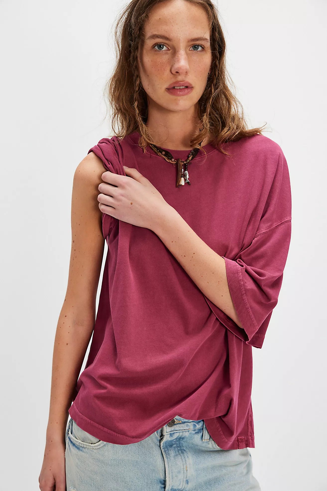 Woman wearing a loose-fitting maroon top with rolled-up sleeves on a white background