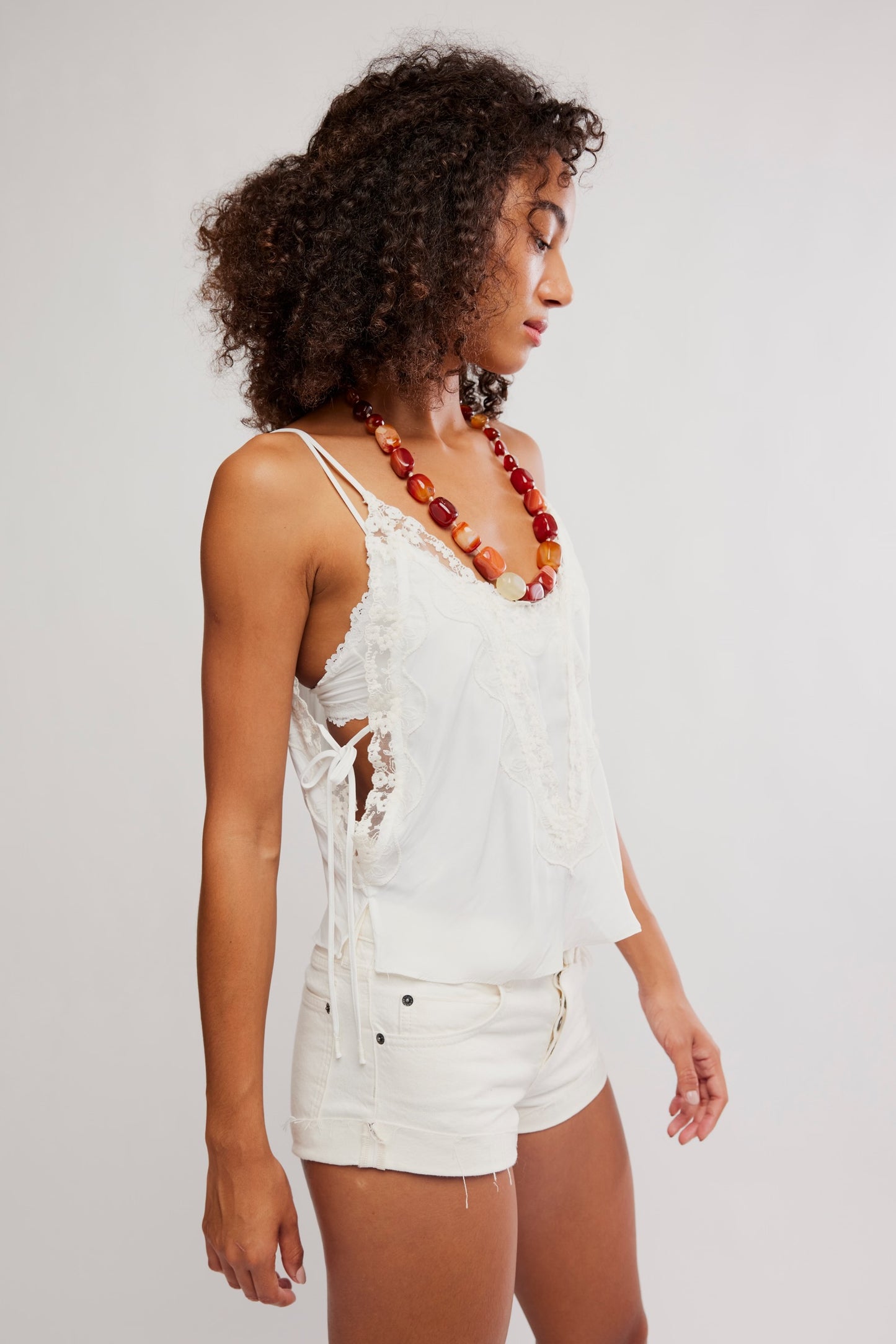 Woman wearing a white lace top and shorts with a red beaded necklace on a plain background