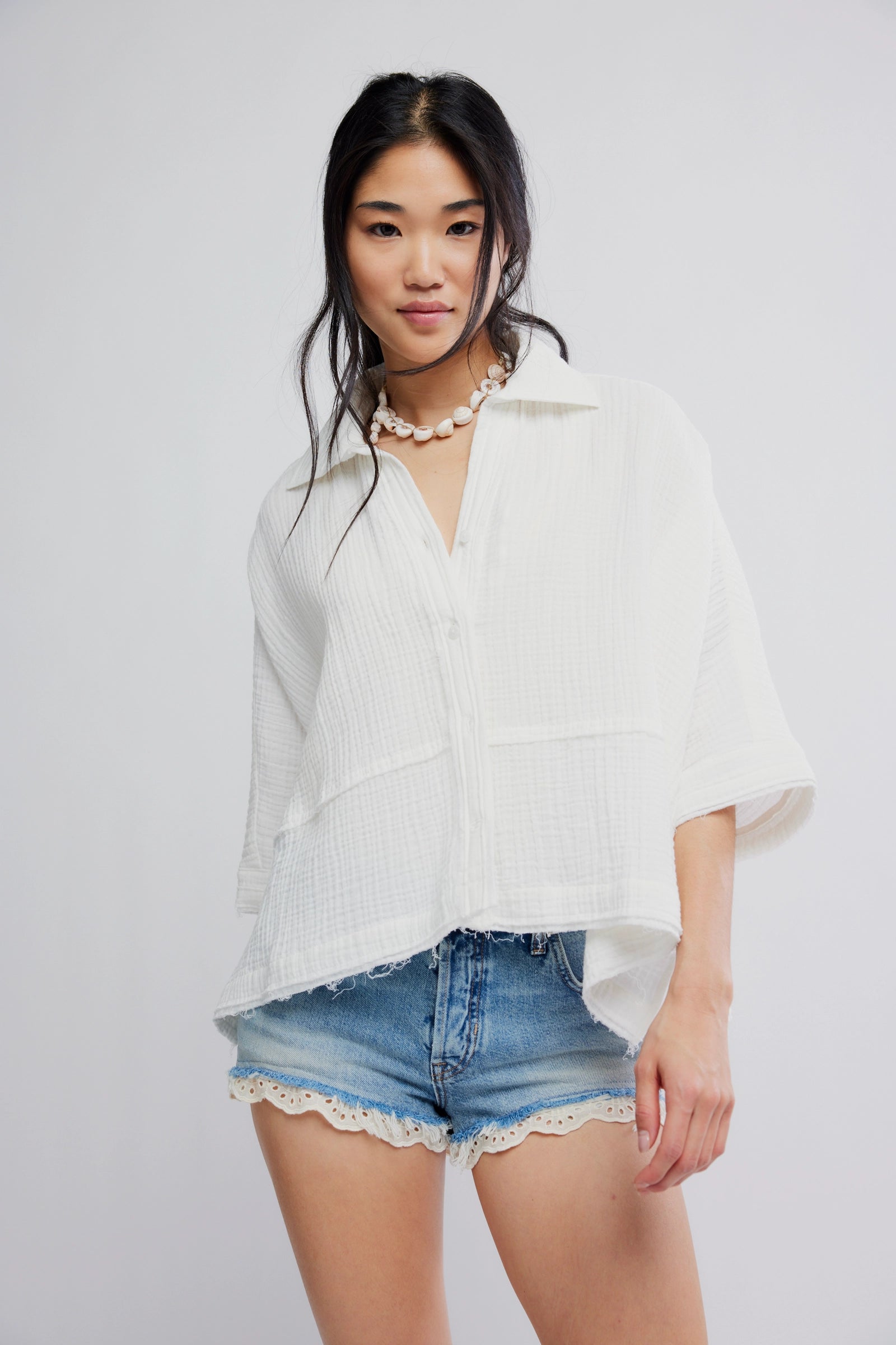 Woman wearing a white blouse and denim shorts on a plain background