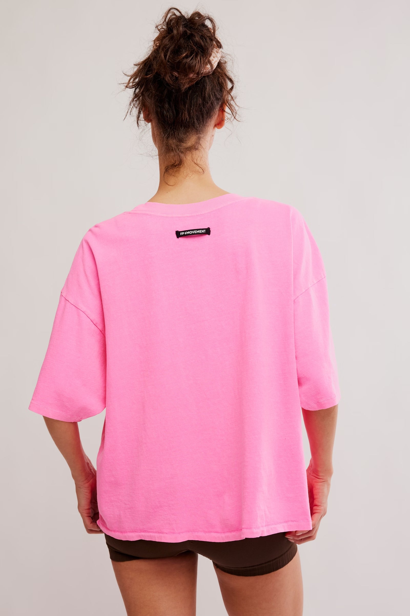 Model wearing Pink Top with brown biker shorts facing backwards