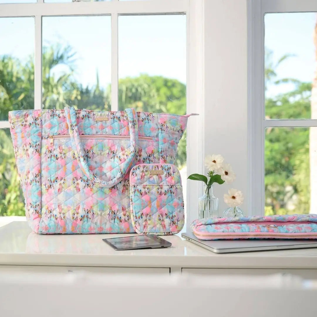 Floral-patterned bags on a desk with a laptop and phone, window in the background