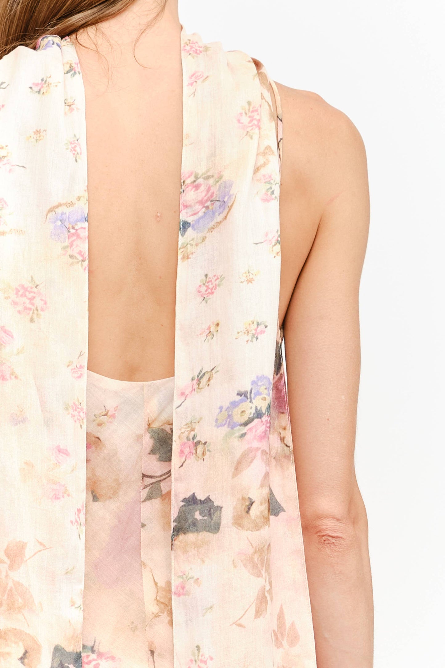 Close-up back view of a model wearing a sleeveless, open-back sheer top or dress in a light blush pink color with a watercolor floral print in soft pastel tones.