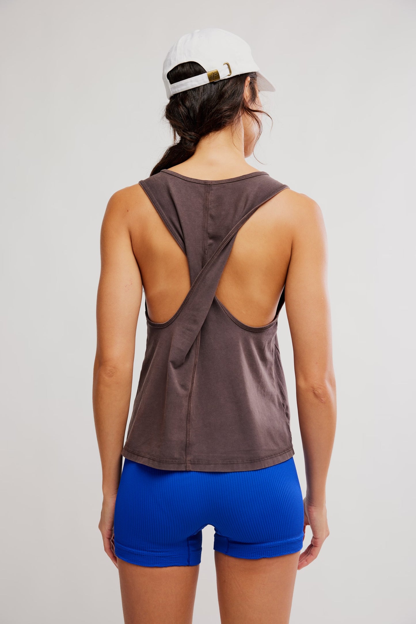 Person wearing a brown tank top with open back and blue shorts on a plain background