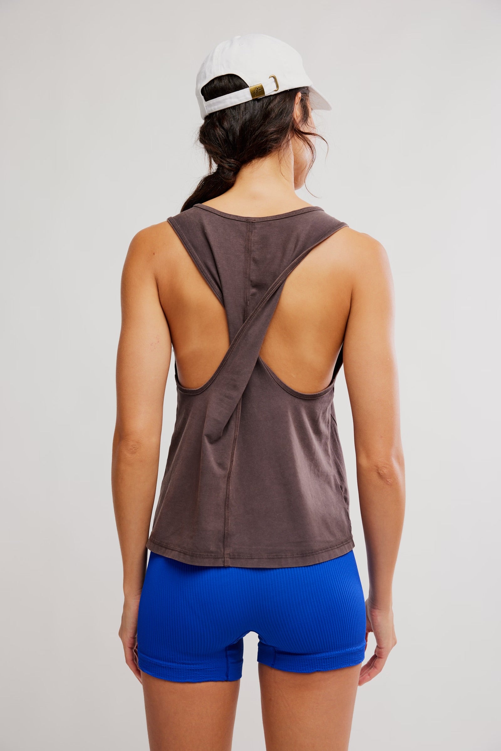 Person wearing a brown tank top with open back and blue shorts on a plain background