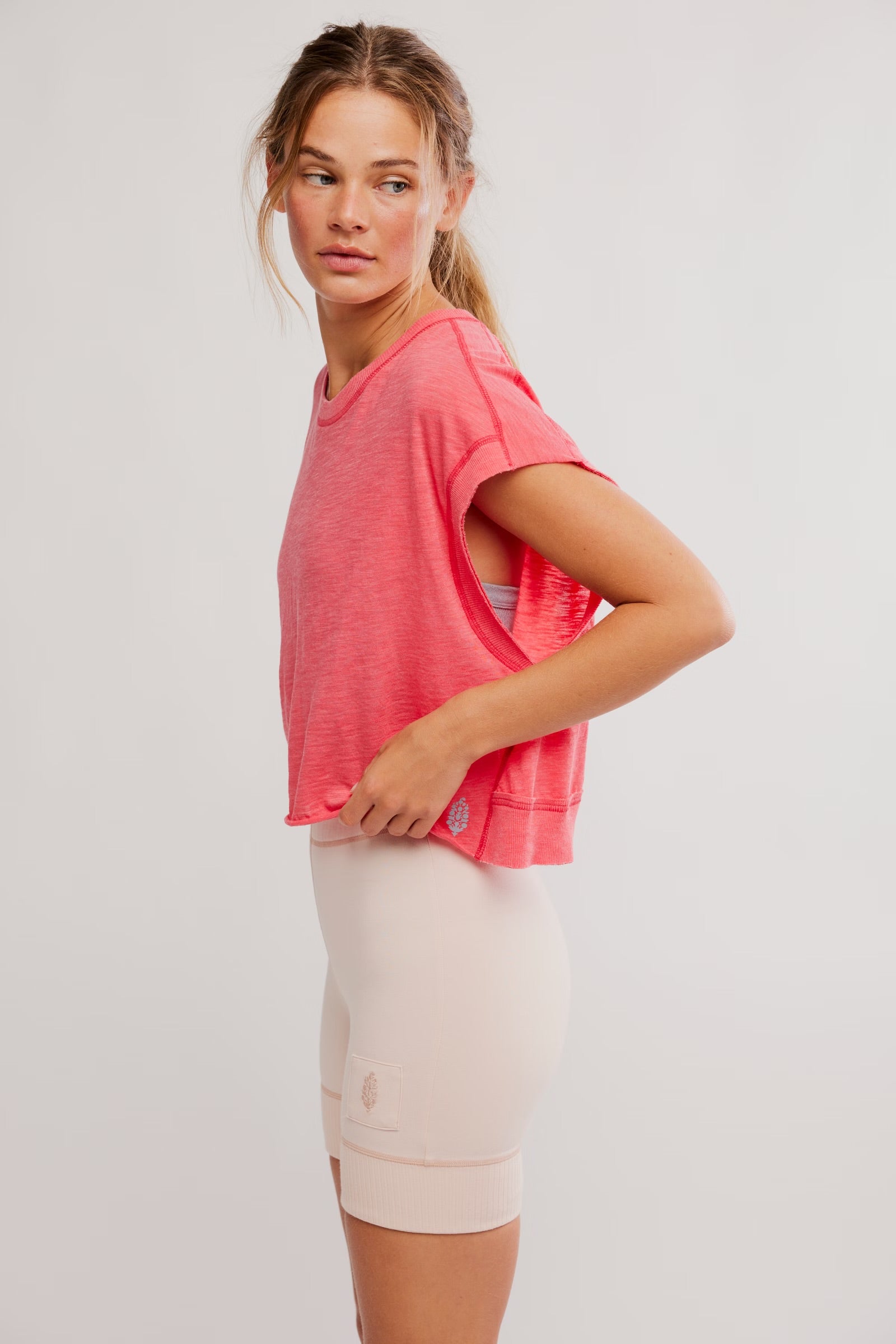 Woman wearing a pink t-shirt and beige shorts on a white background