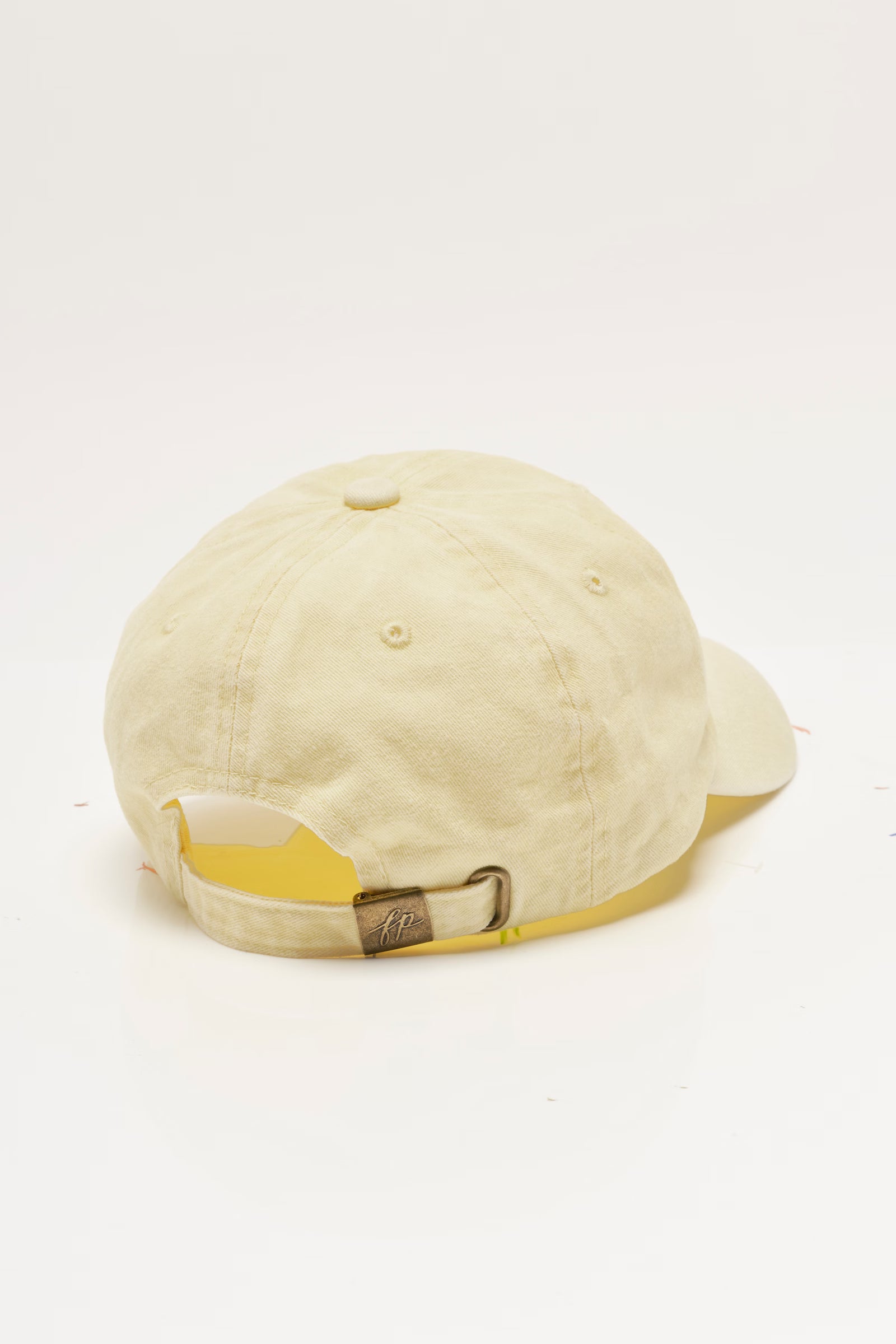 A light cream-colored cotton baseball cap shown from the back, featuring a matching cream fabric band with a small gold metal buckle.