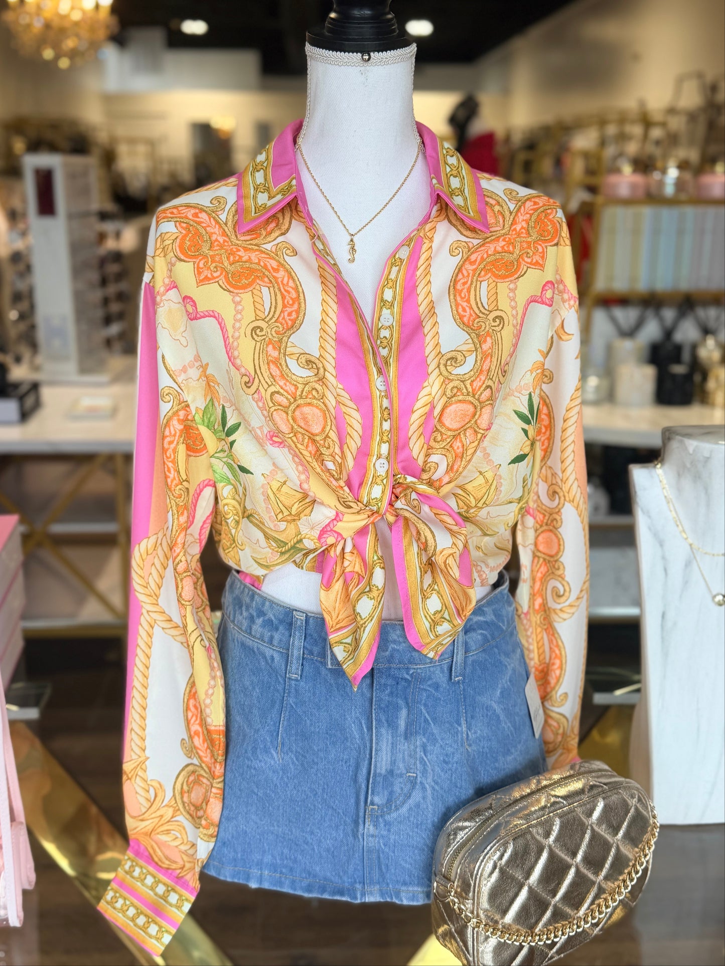 Mannequin wearing a patterned blouse and denim shorts with a handbag in a store setting.