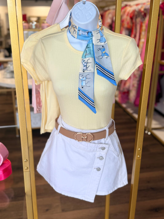 Mannequin wearing a yellow top, white skirt, and blue scarf with a store interior background.