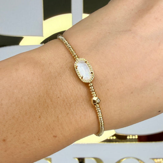 Gold bracelet with a white stone on a wrist against a decorative background