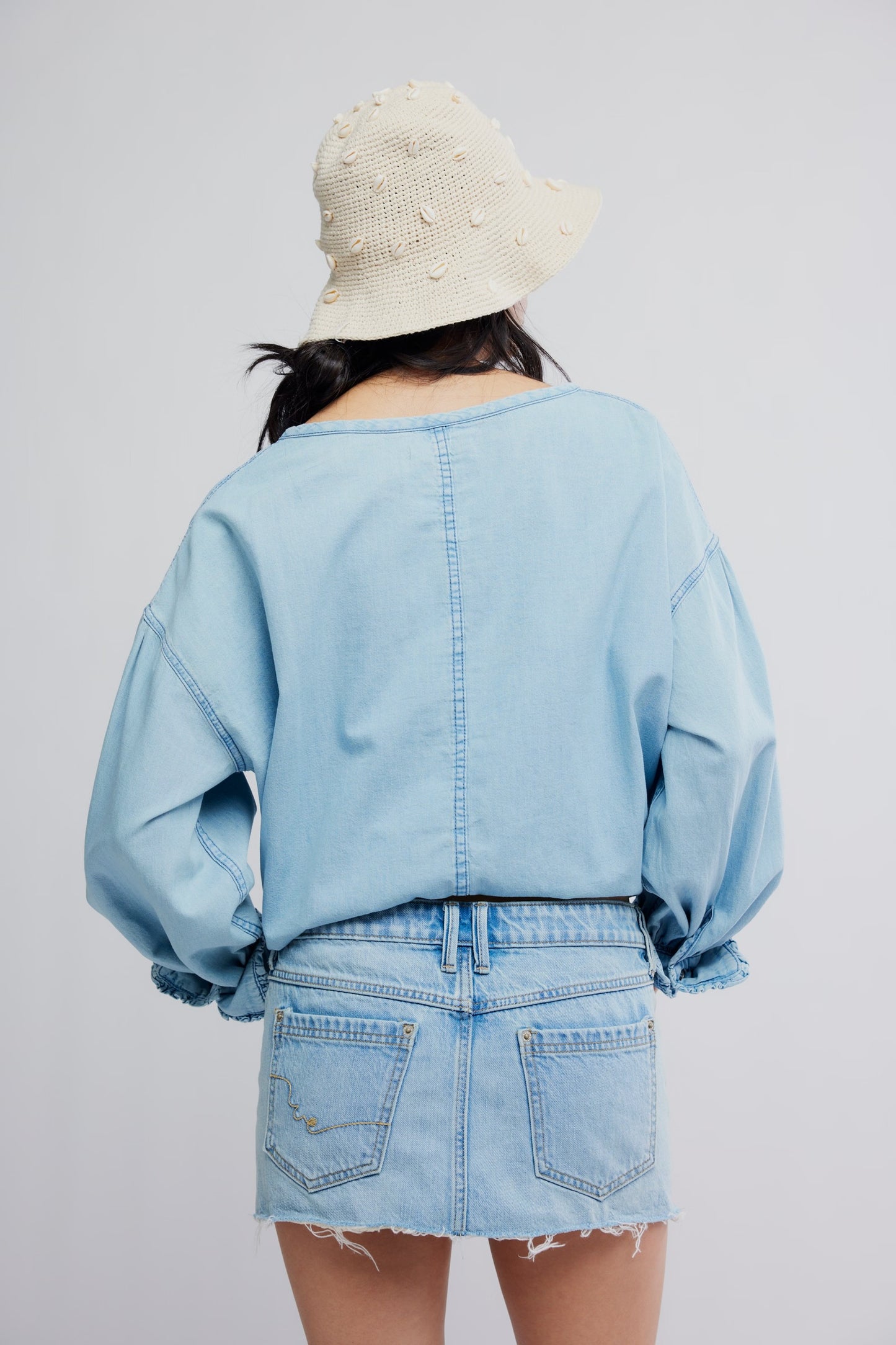 Person wearing a light blue denim jacket and skirt with a white textured hat on a plain background