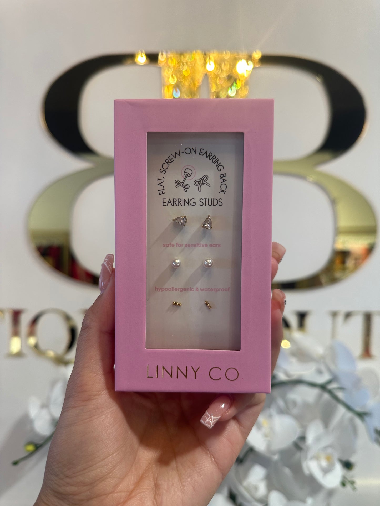 Pink box of earrings held by a hand with a blurred decorative background