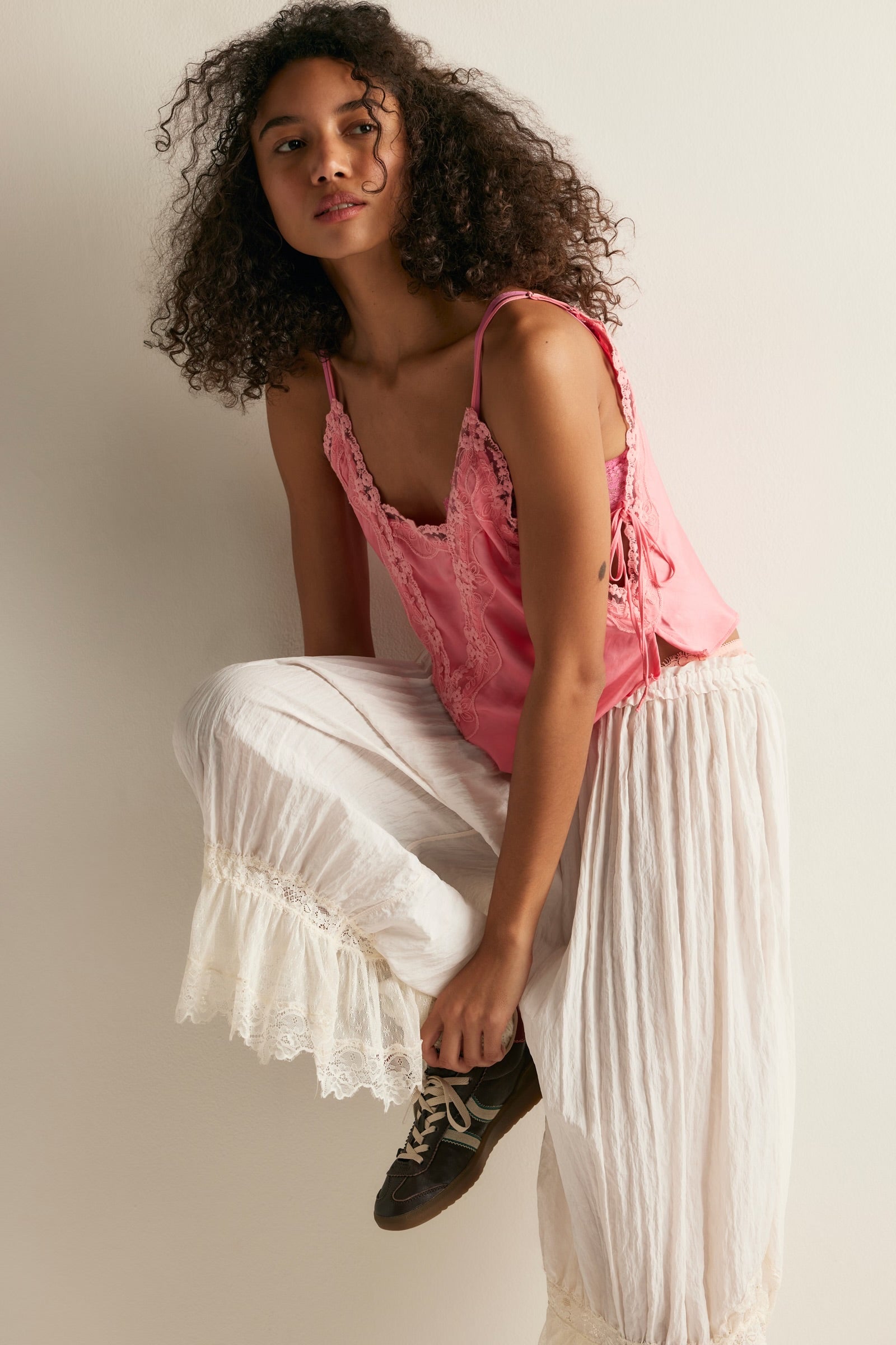 women wearing pink lace tank top standing to side with one leg up