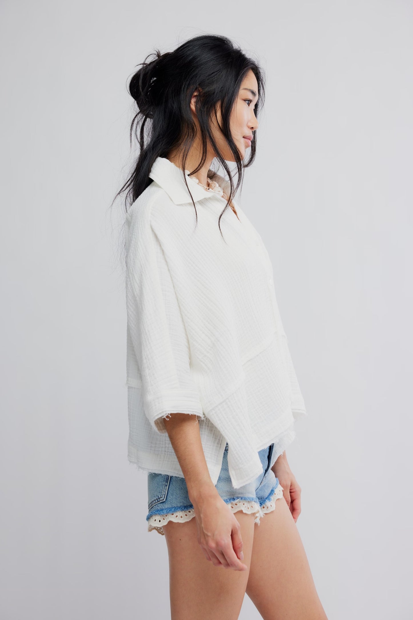 Woman wearing a white shirt and denim shorts on a plain background