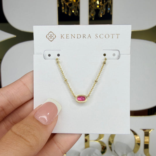 Gold necklace with a red gemstone on a Kendra Scott card held by a hand.