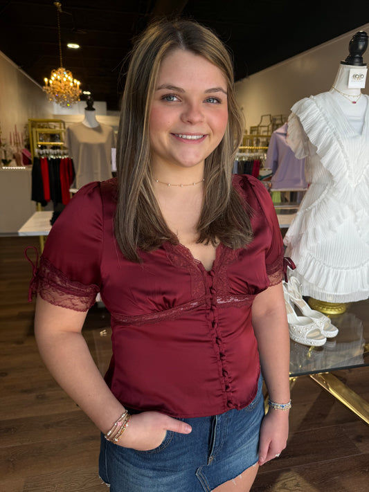 Britique Boutique model wearing burgundy silk top with store background. 