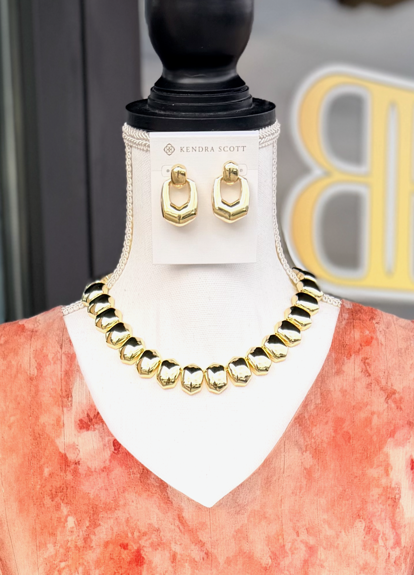 Gold necklace and earrings on a mannequin with Kendra Scott branding.