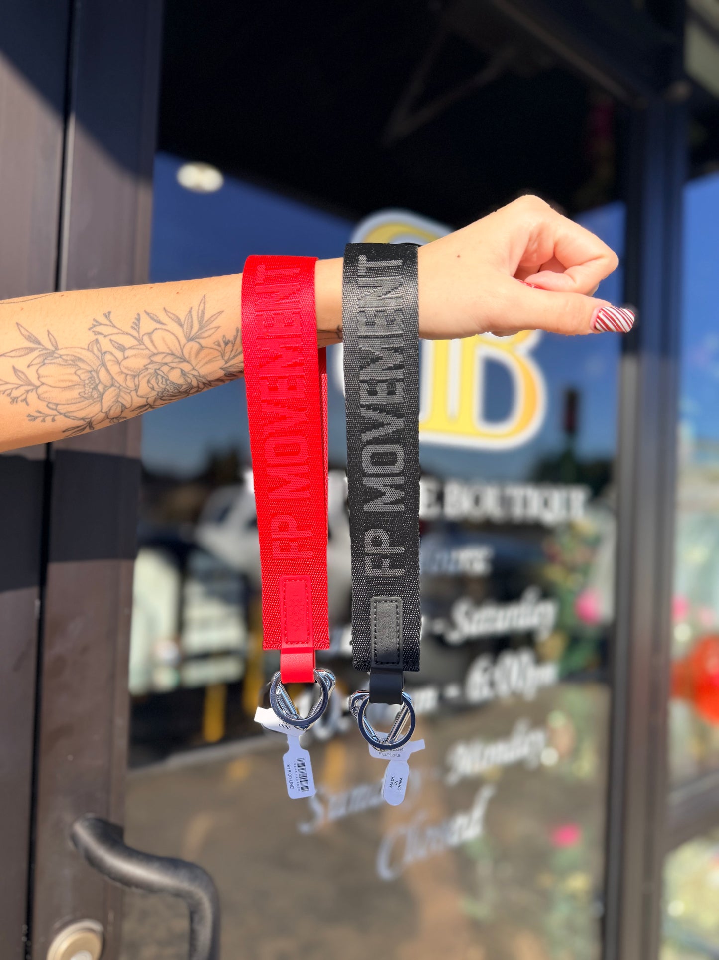 Two wristbands, one red and one gray, with 'FP Movement' branding, held against a blurred store exterior.