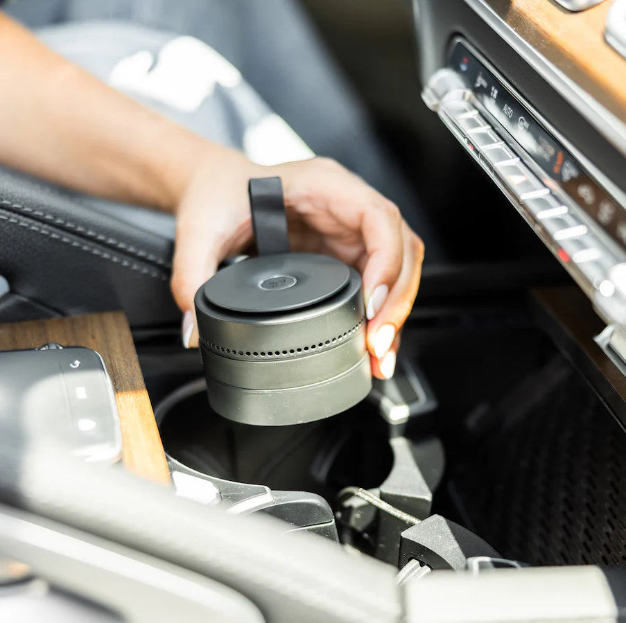 Person placing a black cylindrical pura device into a car cup holder.