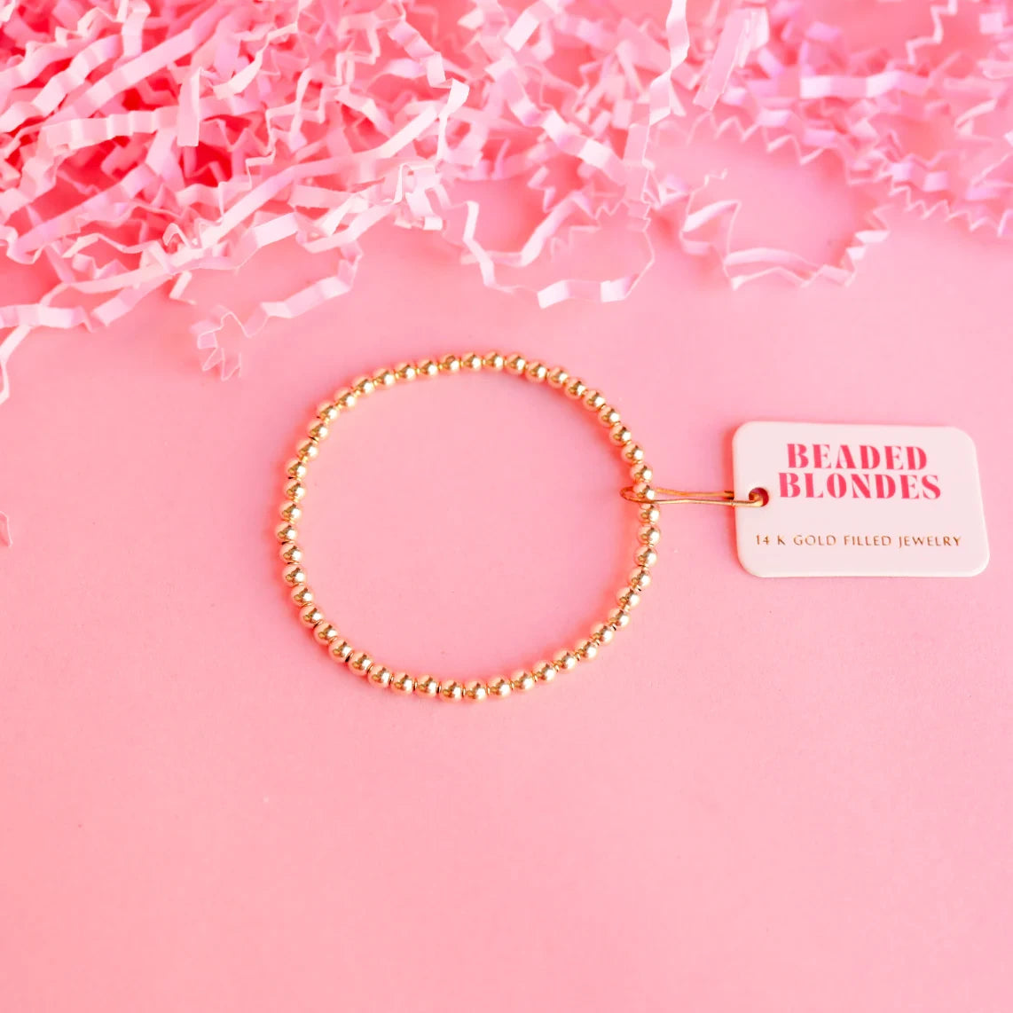 Beaded Blondes 4mm Gold Bracelet arranged with a brand tag on a pink background.