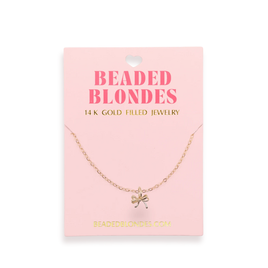 Beaded Blondes Bow Charm Necklace displayed on a pink jewelry card.