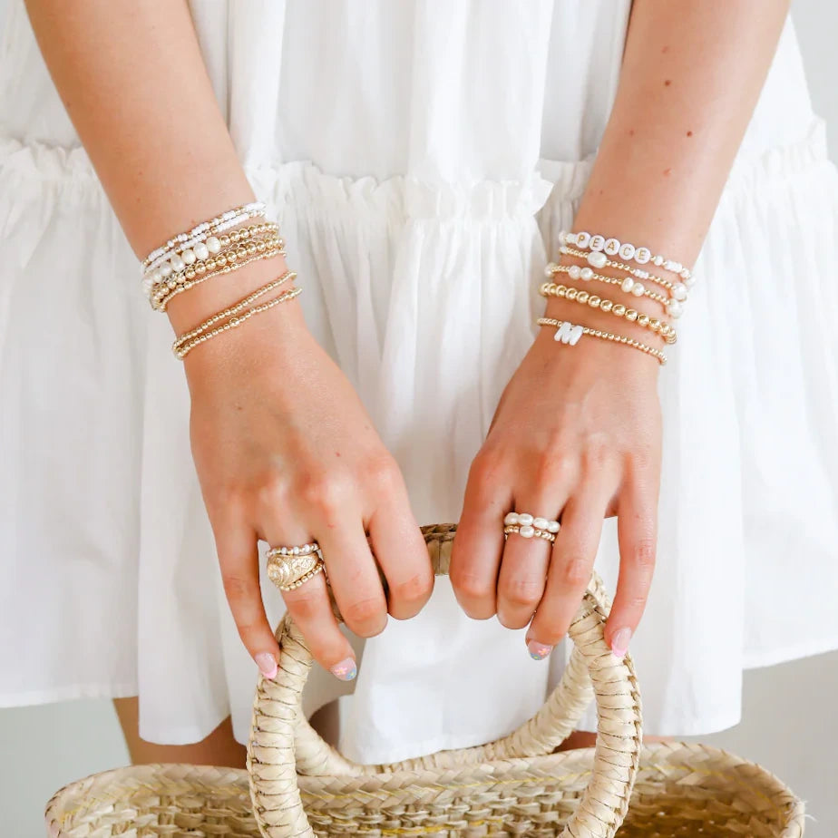 Pearl rings and layered pearl-and-gold bracelets styled with a white dress and woven bag.