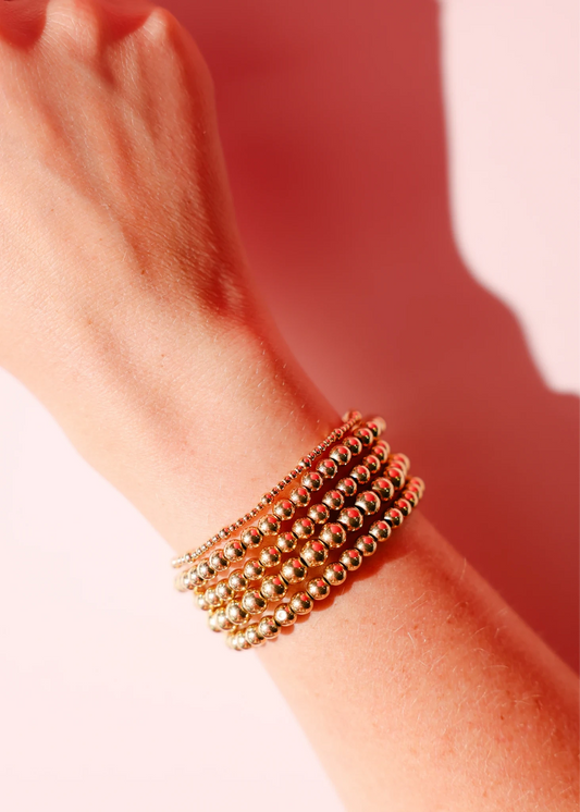 Stack of gold beaded bracelets on a wrist.
