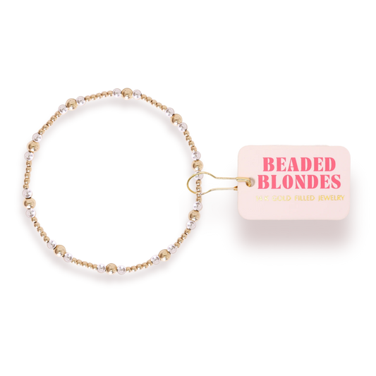 Beaded Blondes Dainty Sutton Bracelet in Gold with Silver beside a pink jewelry tag.