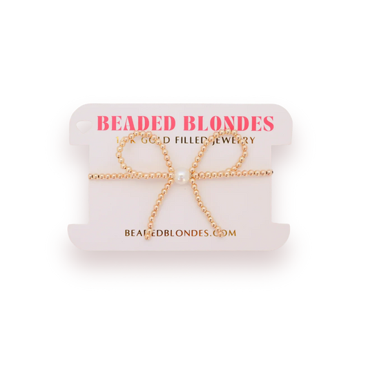 Beaded Blondes Gold Bow Bracelet displayed on a pink jewelry card.