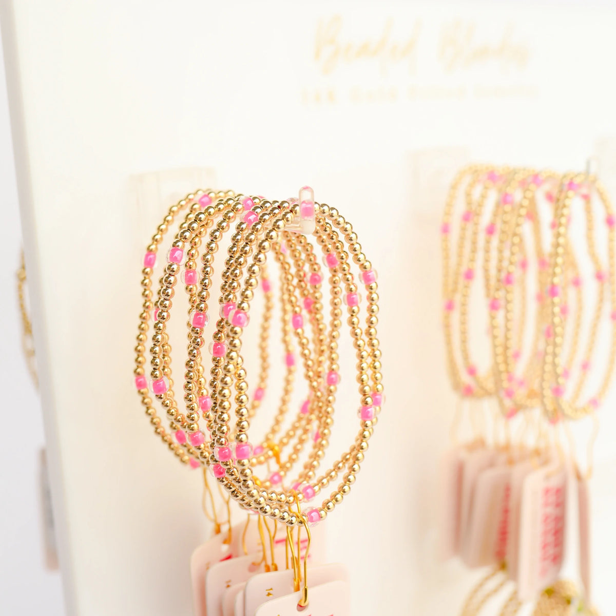 Pink and gold beaded bracelets hanging together on a jewelry display.