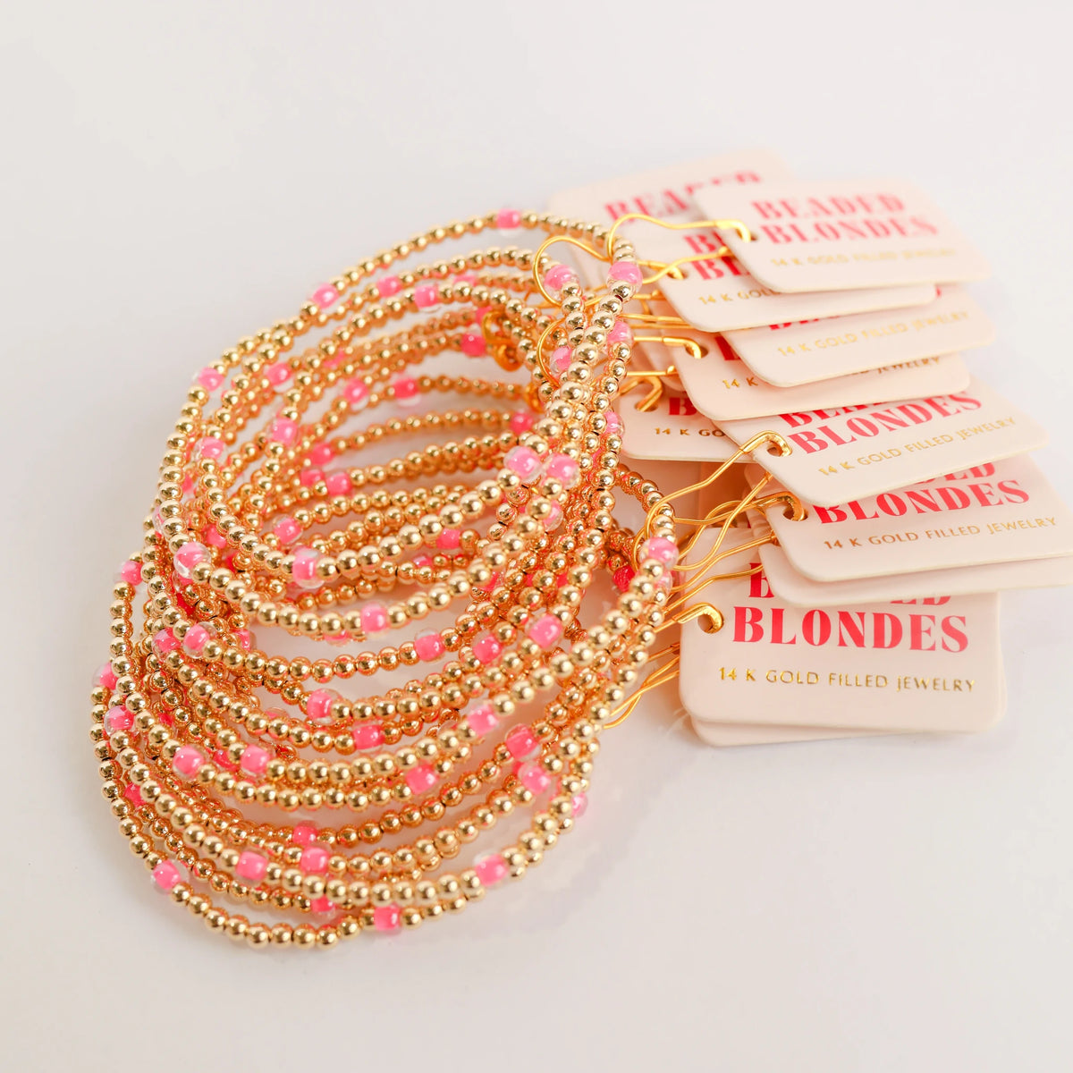 A group of hot pink and gold beaded bracelets arranged with Beaded Blondes display cards.