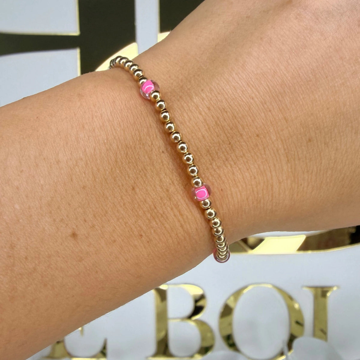 Beaded Blondes Hot Pink Poppi Bracelet with pink accents between gold beads, shown on a wrist.
