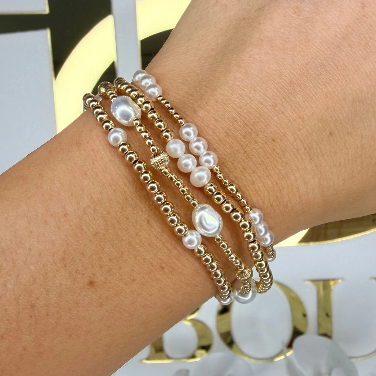 Pearl and gold beaded bracelets layered together on a wrist in front of the Britique Boutique sign.