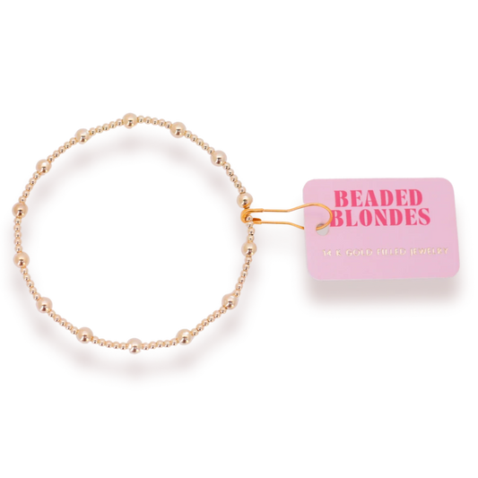 Beaded Blondes June Bracelet in Gold beside a pink jewelry tag.