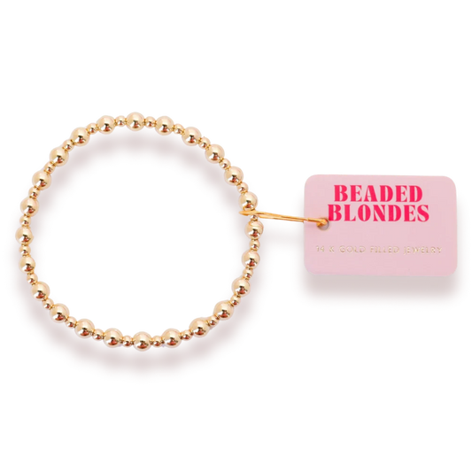 Beaded Blondes Katy Bracelet in Gold beside a pink jewelry tag.