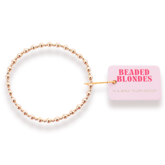 Beaded Blondes Katy Mini Bracelet in Gold beside a pink jewelry tag.