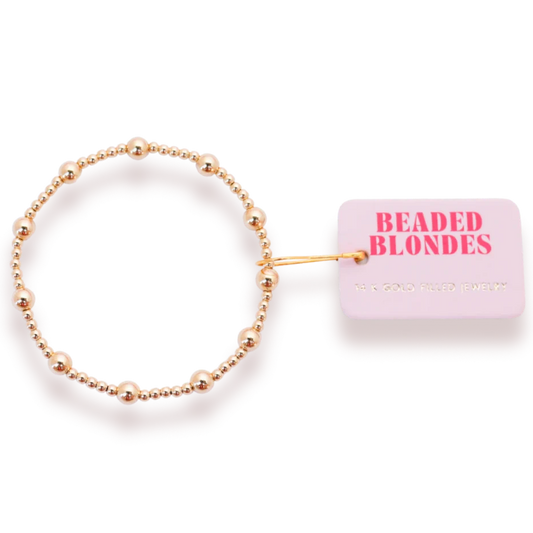 Beaded Blondes Lively Bracelet in Gold beside a pink jewelry tag.