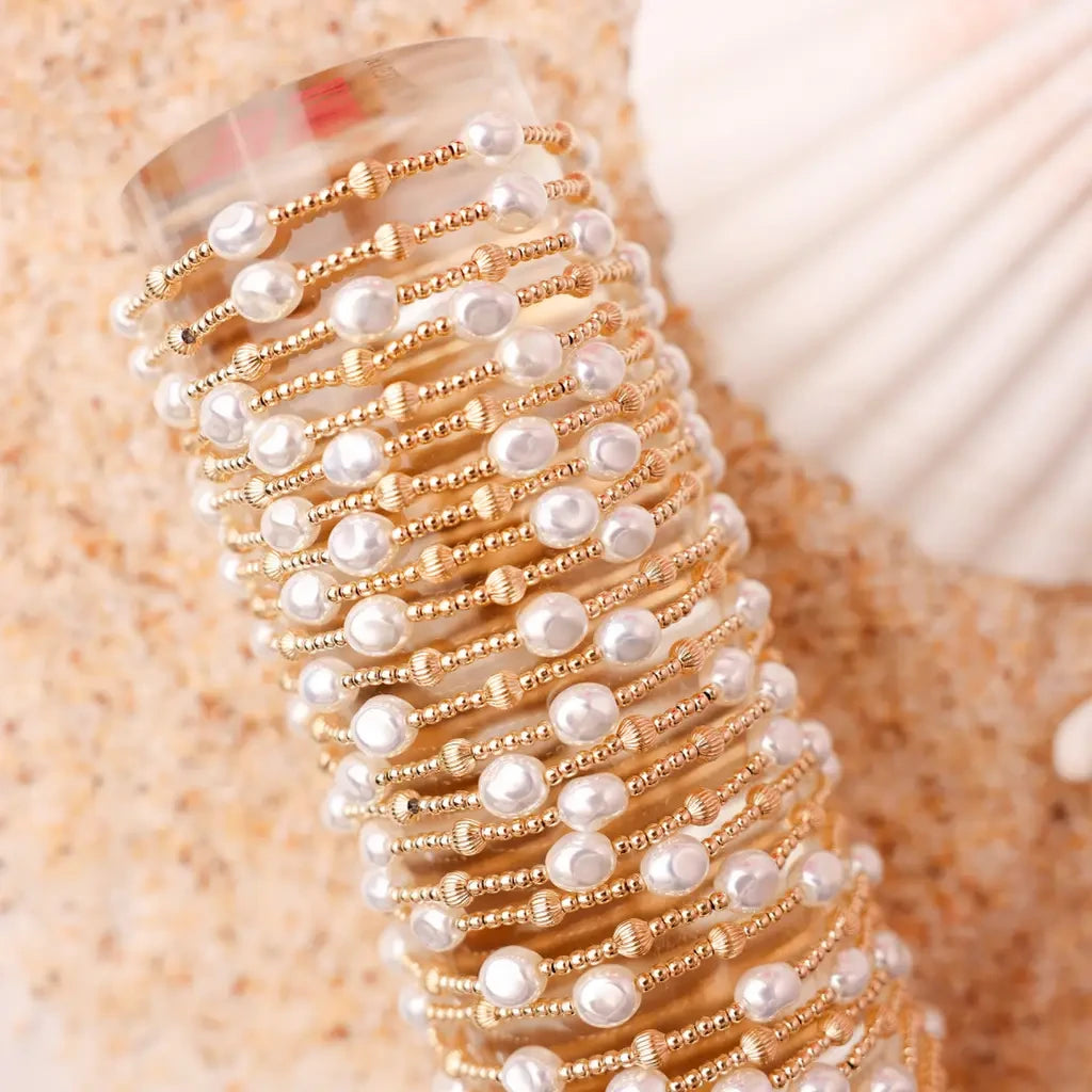 A stack of pearl and gold beaded bracelets arranged on a wrist beside a woven accessory.