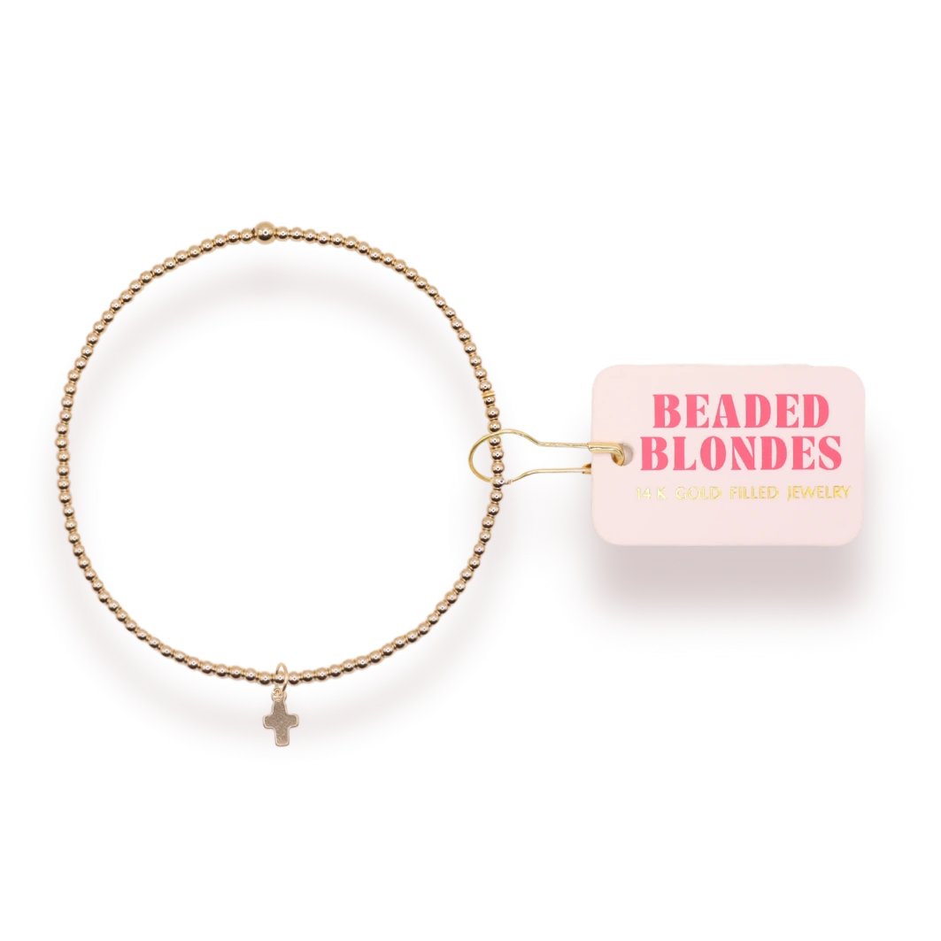 Beaded Blondes Mini Cross Charm Bracelet on Gold beside a pink jewelry tag.