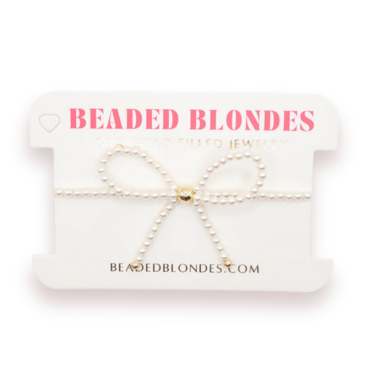 Beaded Blondes Pearl Bow Bracelet with a white pearl bow and gold details on a display card.