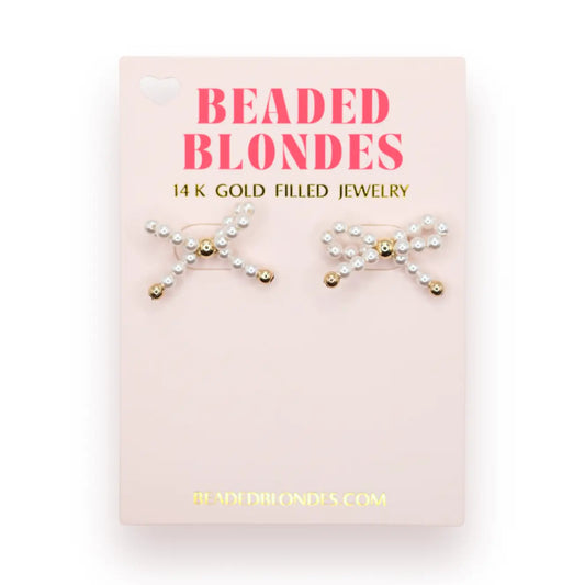 Beaded Blondes Pearl Bow Earrings with white pearl bows and gold center details on a pink jewelry card.