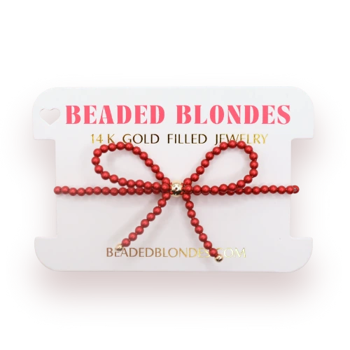 Beaded Blondes Red Bow Bracelet displayed on a pink jewelry card.