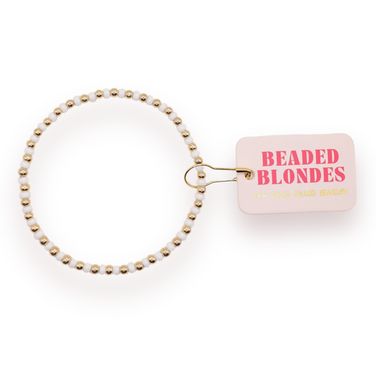 Beaded Blondes White Demi Bracelet with white glass accents and gold beads beside a pink brand tag.