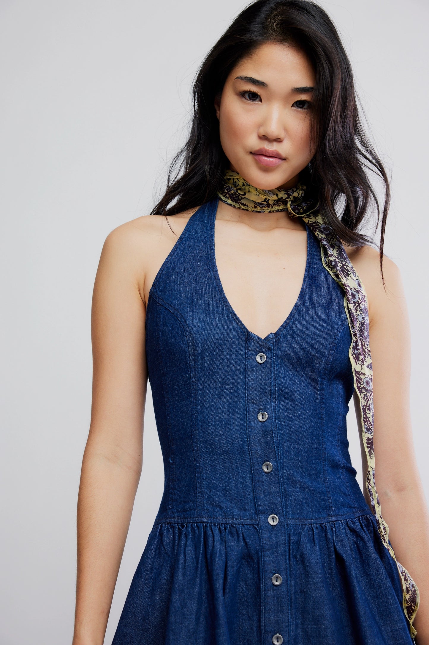 Woman wearing a blue dress with a patterned scarf around her neck against a plain background