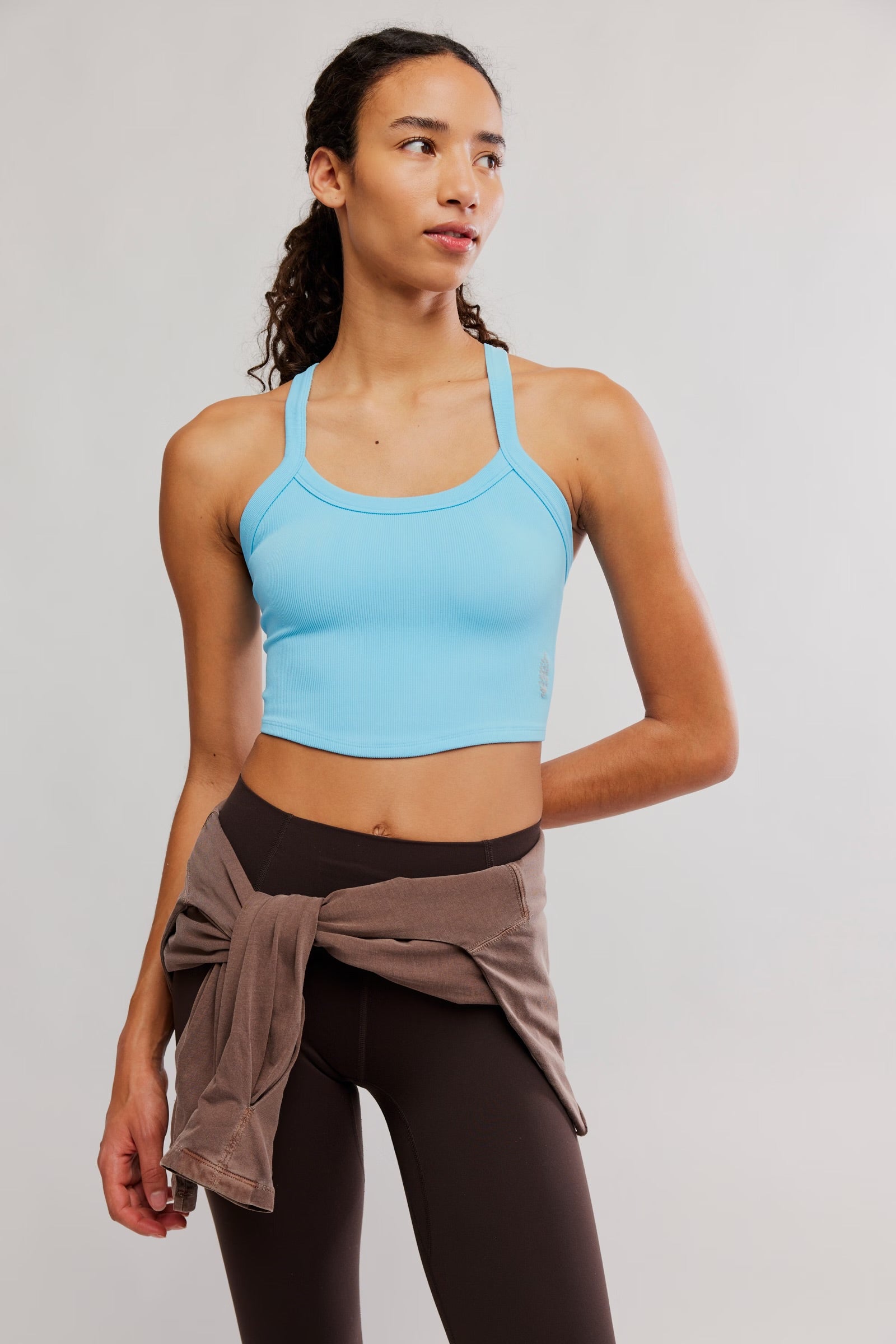 Woman wearing a blue sports bra and brown leggings on a plain background