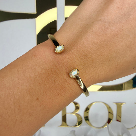 Gold bracelet with a central gemstone on a wrist, with a blurred background featuring 'Boutique' text.