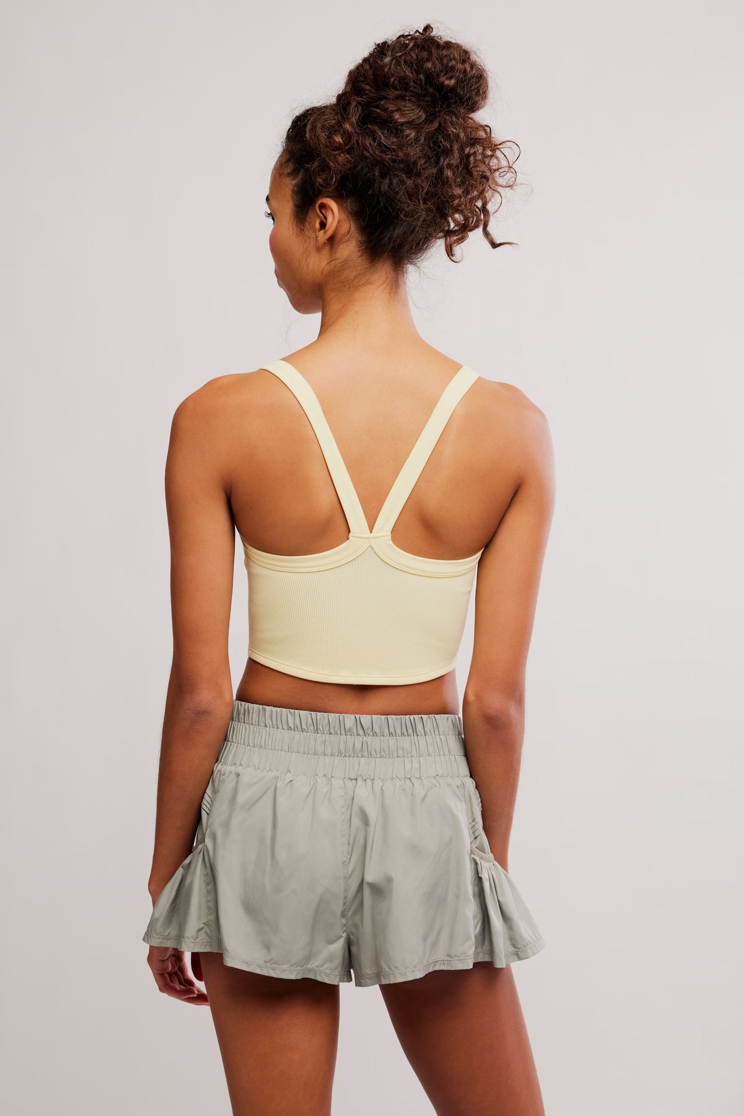 Person wearing a light yellow sports bra and gray shorts on a plain background