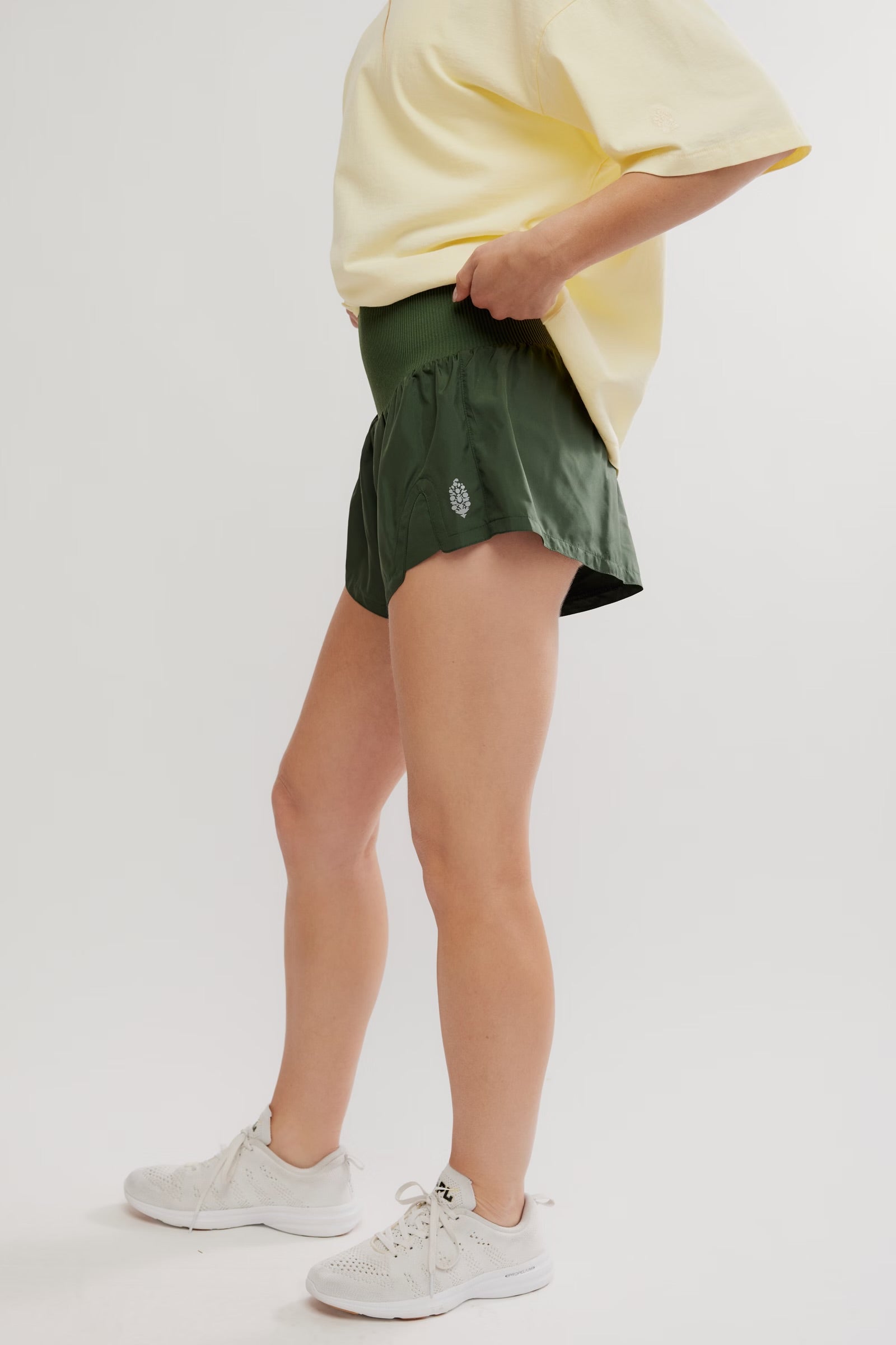 Person wearing a yellow oversized shirt, green shorts, and white sneakers on a light gray background
