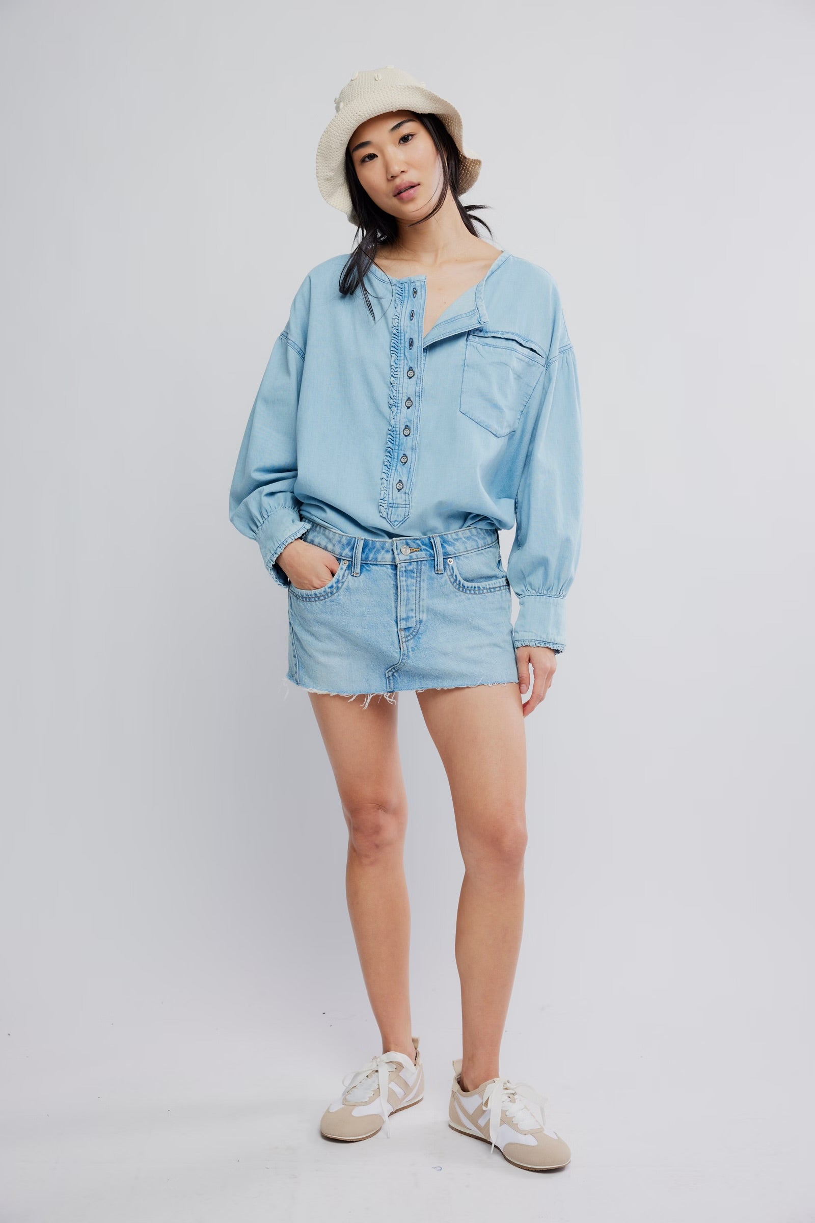 Person wearing a light blue denim outfit with a white hat on a plain background