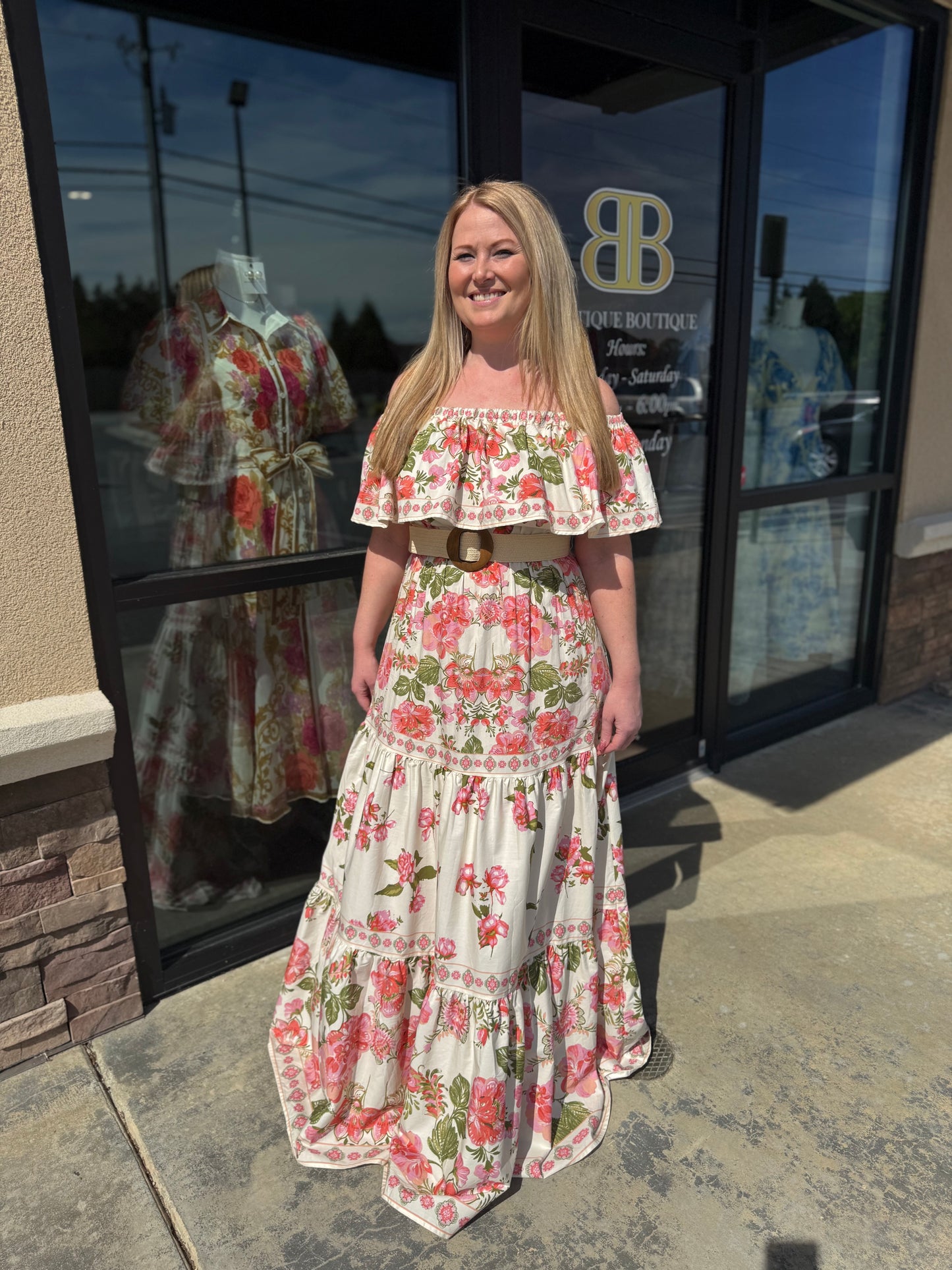 Woman in a floral dress standing outside a building with large glass doors.